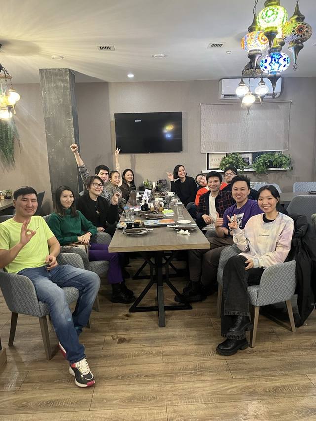 A group around a long café table, smiling and waving at the camera