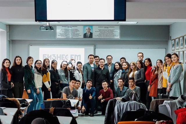 A group photo in a classroom, with Business FM on the screen